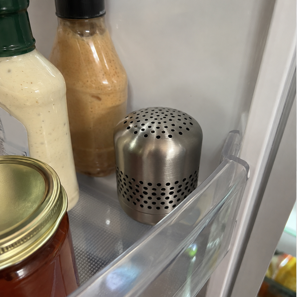 Kursi refrigerator deodorizer positioned upright beside condiments on a refrigerator door shelf