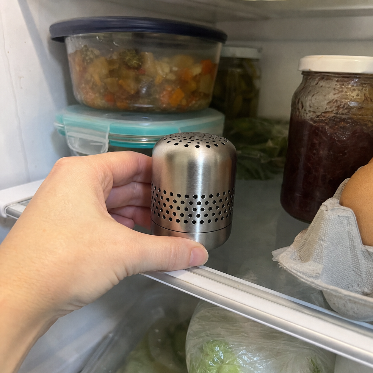 Kursi deodorizer being placed inside a refrigerator beside leftovers and eggs